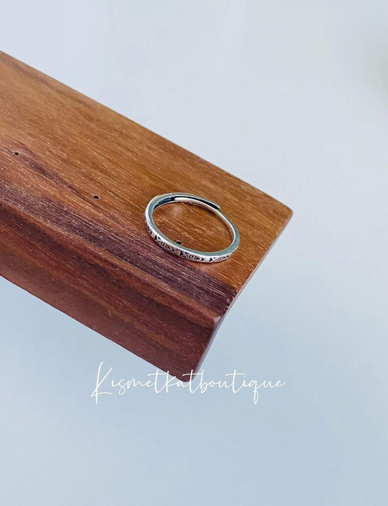 May include: A silver ring with a delicate design on a wooden surface.