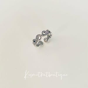 May include: Silver ring featuring a design of multiple swirling circles.