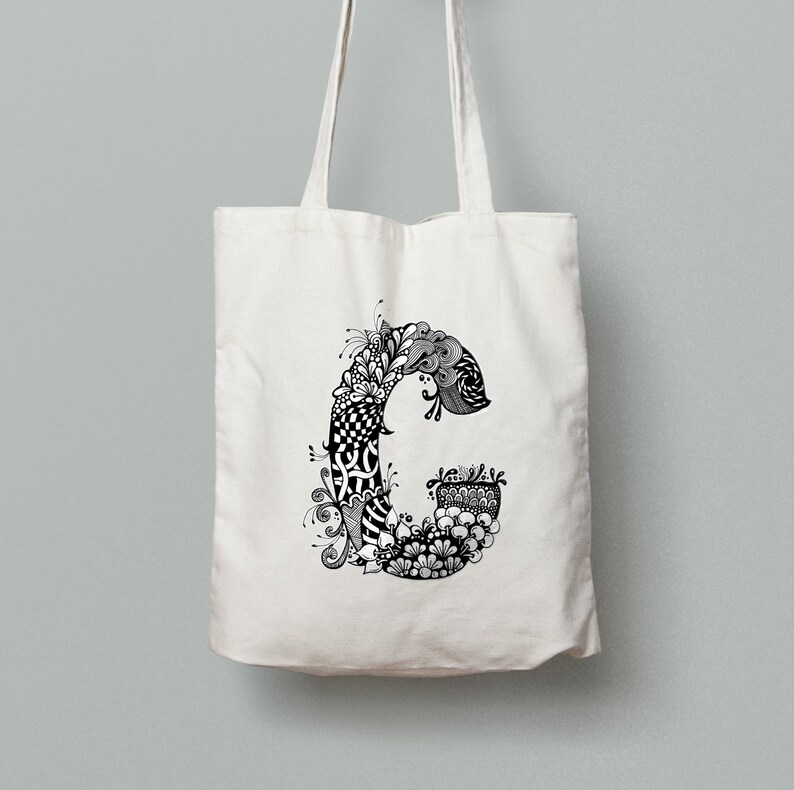 K&ouml;nnte beinhalten: Eine wei&szlig;e Canvas-Tragetasche mit einer schwarz-wei&szlig;en Kritzelei des Buchstabens "C" auf der Vorderseite.