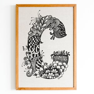 K&ouml;nnte beinhalten: Eine gerahmte Schwarzwei&szlig;illustration des Buchstabens C mit komplizierten floralen und geometrischen Mustern. Das Kunstwerk befindet sich auf einem Leinenhintergrund und ist mit "Huerr" signiert.