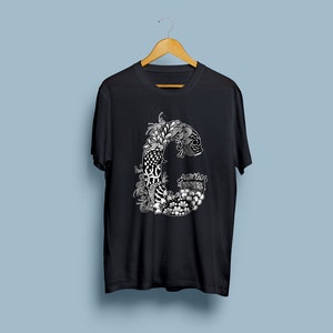 K&ouml;nnte beinhalten: Schwarzes T-Shirt mit einem wei&szlig;en Grafikdruck des Buchstabens "C" in einem komplizierten floralen Design.