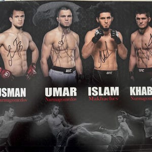 Puede incluir: Un póster con cuatro luchadores de la UFC: Usman Nurmagomedov, Umar Nurmagomedov, Islam Makhachev y Khabib Nurmagomedov. Cada luchador está sin camiseta y firmado. El póster incluye el logotipo de la UFC y los nombres de los luchadores.