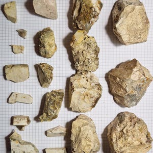 Könnte beinhalten: Eine Ansammlung von unterschiedlich großen, grob behauenen Steinen und Felsen. Die Steine weisen neutrale Farben wie Beige, Hellbraun und Weiß auf, einige zeigen auch Gelb- und Brauntöne. Die Anordnung erfolgt auf einem Raster.