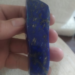 May include: A deep blue lapis lazuli stone with gold pyrite inclusions. The stone is smooth and polished, and has a slightly irregular shape.