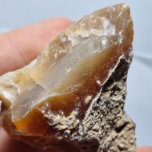 Può includere: Un ciottolo di agata ruvido, di colore marrone e bianco, con un centro traslucido. Il ciottolo ha una forma naturale irregolare e una superficie ruvida e testurizzata.
