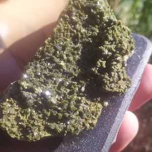 May include: A close-up of a green rock with sparkly crystals. The rock is on a black surface.