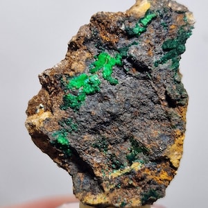 Op de afbeelding: Een ruwe, donkergrijze rots met vlekken van felgroene en gele mineralen.