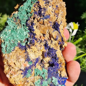Peut inclure: Un spécimen de roche naturelle brute avec un mélange de couleurs bleues, vertes et brunes. La roche a une surface rugueuse et texturée et est recouverte de petits cristaux.
