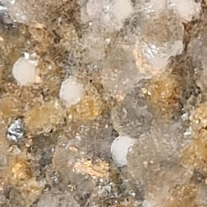 May include: Close-up of a textured surface with a mix of colors, including beige, brown, and white. The surface has a granular appearance with small, rounded, white and clear crystalline formations.