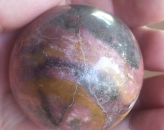 May include: A polished, spherical gemstone with a mix of colors including pink, brown, and gold. The stone has natural veining and a glossy finish. This decorative sphere is a unique home decor item.