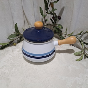 May include: A white enamel saucepan with a blue and white striped design and a wooden handle. The saucepan has a dark blue lid.