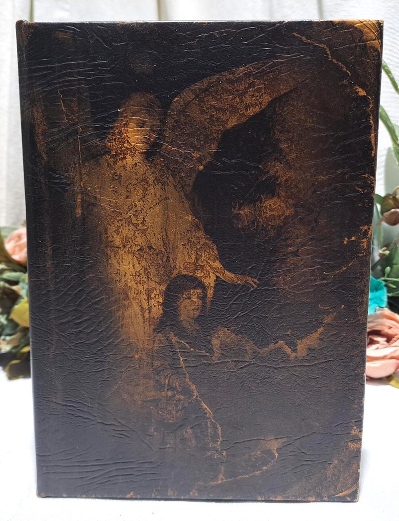 May include: A vintage book with a dark brown, textured cover. The cover features a sepia-toned illustration of an angel and a person. The artwork is detailed, with visible brushstrokes and shading, creating a classic, antique aesthetic.