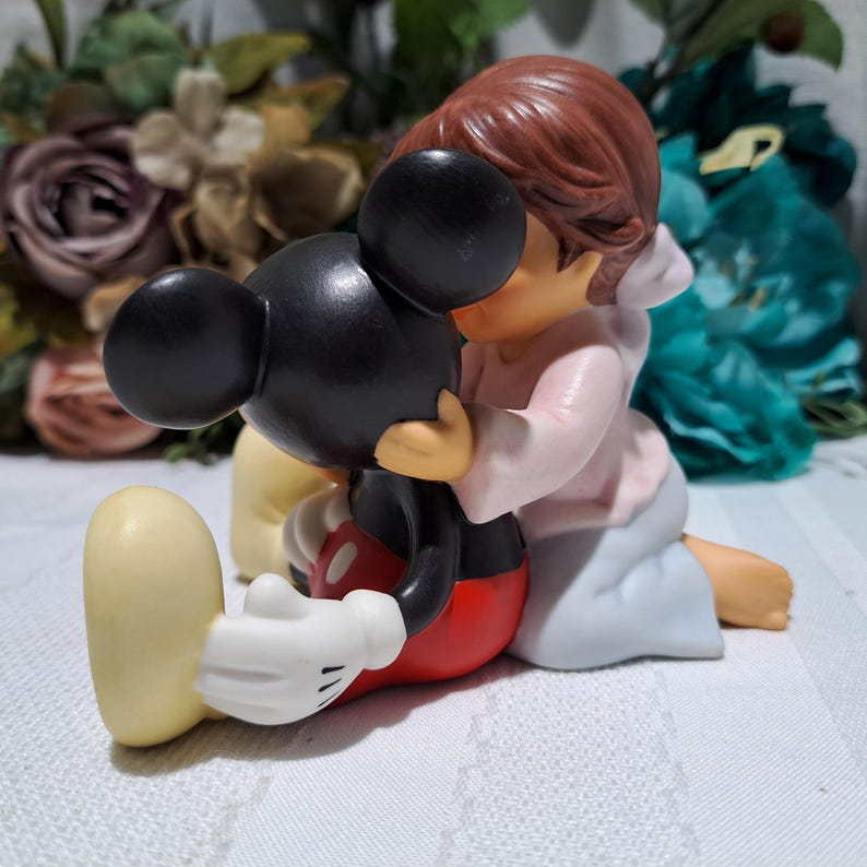 Pode incluir: Uma estatueta de cer&acirc;mica retratando Mickey Mouse sendo abra&ccedil;ado por uma figura em um top rosa e saia azul. Mickey Mouse &eacute; preto com shorts vermelhos, sapatos amarelos e luvas brancas.