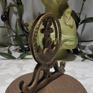 May include: A brass napkin holder with an anchor design. The holder has a round base and a decorative top with a rope design.