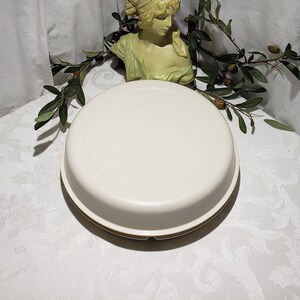 May include: A white ceramic cake stand with a raised rim and a smooth, glossy finish. The stand is round and has a diameter of approximately 12 inches.