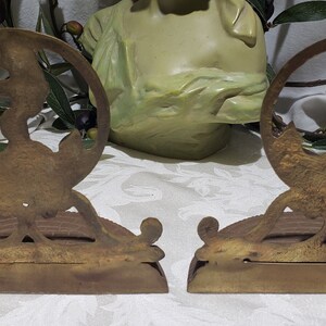 May include: A pair of antique brass bookends featuring a stylized design of a woman holding a torch. The bookends are in good condition with some signs of age and wear.