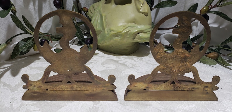 May include: A pair of antique brass bookends featuring a stylized design of a woman holding a torch. The bookends are in good condition with some signs of age and wear.