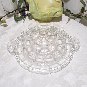 May include: A clear glass tiered serving tray with a decorative design. The tray has two handles and is perfect for serving snacks or desserts.
