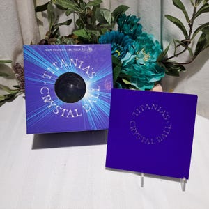 May include: A purple box with the text "TITANIA'S CRYSTAL BALL" and a black crystal ball. The box has a radiating light design. A second purple box with the same text is also present.
