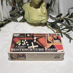 May include: A vintage Scrabble Sentence Cube Game box with a white background and red, white, and blue accents. The box features a photo of a couple playing the game. The text on the box reads "Scrabble Sentence Cube Game".