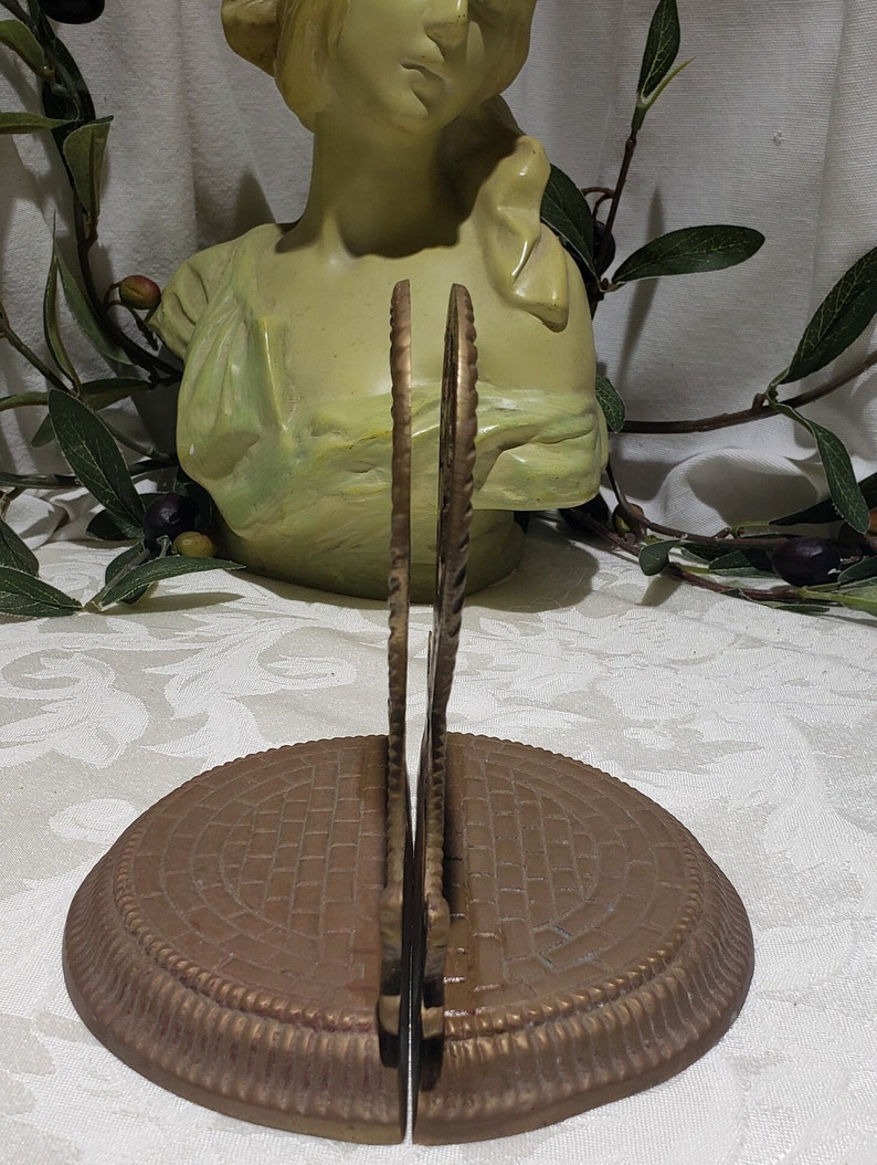 May include: A pair of antique brass bookends with a decorative design. The bookends have a circular base with a textured pattern and a decorative top with a floral design.
