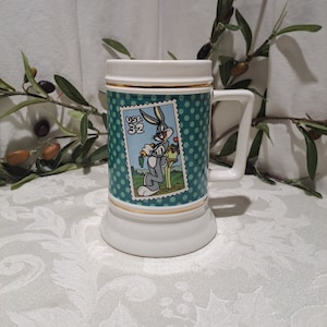 May include: White ceramic mug with a green and white polka dot design. The mug features a Bugs Bunny cartoon character on a postage stamp with the text "USA 32".