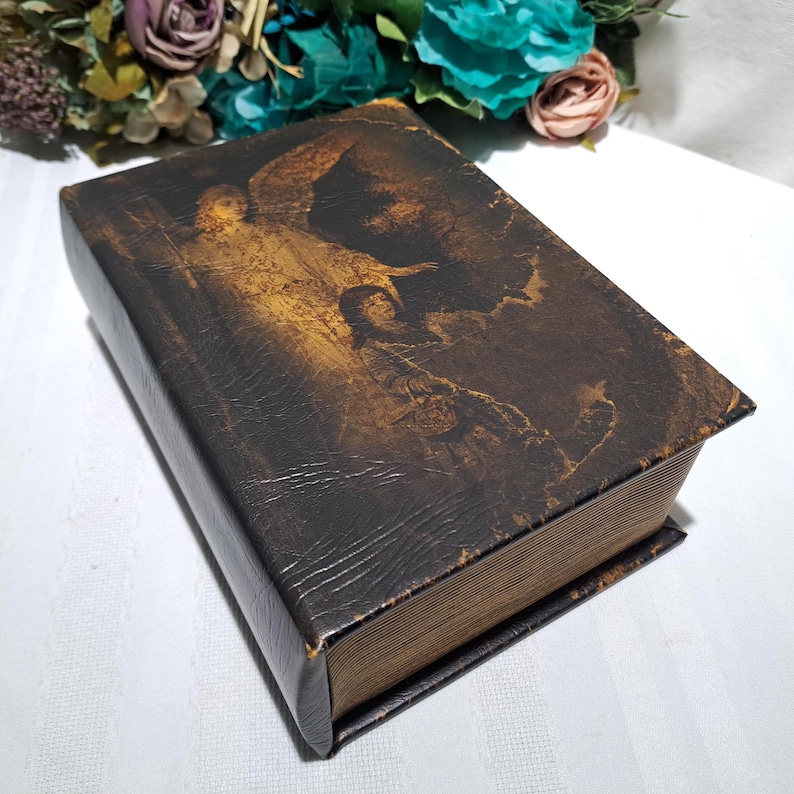 May include: A vintage, rectangular book with a dark brown, textured cover. The cover features a faded, sepia-toned image of an angel and a person. The book's edges are worn, and the pages are aged, giving it a classic, antique appearance.