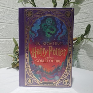 May include: A hardcover book titled Harry Potter and the Goblet of Fire by J.K. Rowling, illustrated by Karl James Mountford. The purple cover features gold foil accents, a green snake and skull graphic, and a colorful scene of characters.