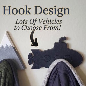 Peut inclure: Un crochet mural en forme de sous-marin noir et un crochet en forme de montagne grise. Le texte au-dessus indique Hook Design Lots Of Vehicles to Choose From! avec une flèche noire pointant vers le sous-marin qui porte un vêtement gris.