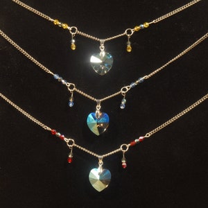 May include: Three silver necklaces with heart-shaped crystal pendants. The top necklace has yellow beads, the middle necklace has blue beads, and the bottom necklace has red beads.