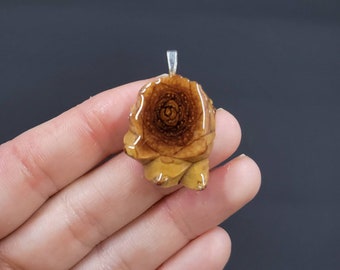 May include: A gold-toned pendant featuring a detailed rose design with a wood grain pattern. The pendant is made of resin and has a silver-toned bail.