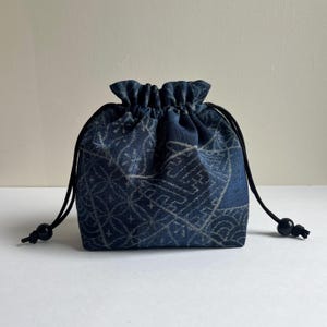 Op de afbeelding: Een witte keramische mok met een zwart handvat en de tekst "But First, Coffee" in een vetgedrukte, zwarte letter. De mok staat op een houten oppervlak. De mok is ongeveer 10 cm hoog.