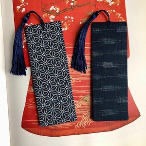 May include: Two blue fabric bookmarks with tassels. One bookmark has a geometric pattern and the other has a striped pattern.