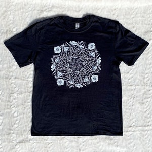 May include: Black t-shirt with a white floral mandala design. The design features a circular pattern of flowers and leaves.
