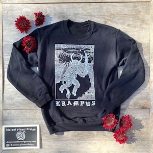 May include: Black sweatshirt with a white print of a Krampus figure with horns and a sack. The text "Krampus" is printed below the figure.