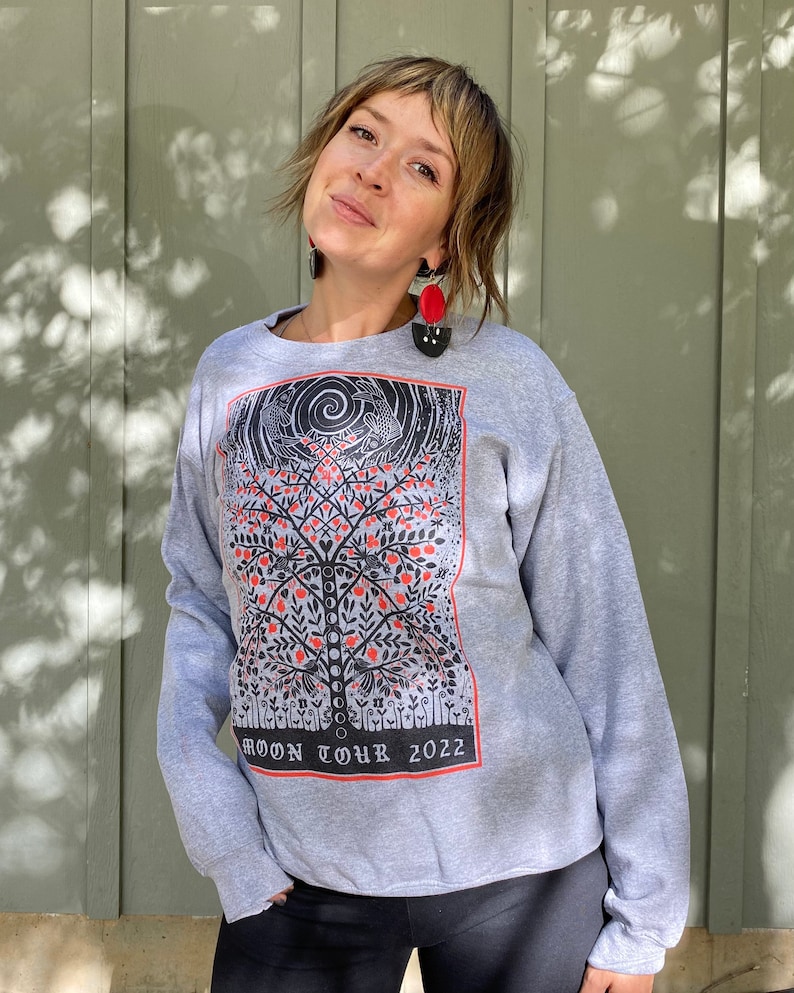 K&ouml;nnte beinhalten: Ein graues Sweatshirt mit einem schwarzen und roten Grafikdruck eines Baumes mit V&ouml;geln und dem Text "MOON TOUR 2022".