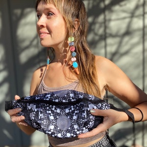 May include: A black and white fanny pack with a psychedelic mushroom and spiral pattern. The fanny pack has a black zipper and a black adjustable strap.