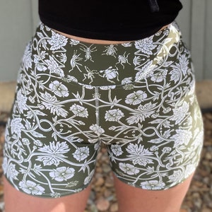 May include: Green athletic shorts with a white floral and insect print. The print features a repeating pattern of flowers, vines, and insects.