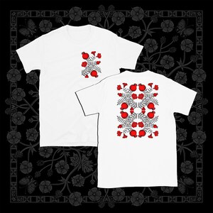 May include: Two white t-shirts with a red pomegranate pattern. The pattern features red pomegranates, green leaves, and white flowers.