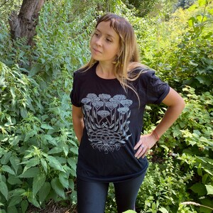 K&ouml;nnte beinhalten: Ein schwarzes T-Shirt mit einem wei&szlig;en Aufdruck einer Gruppe von Schafgarbenbl&uuml;ten. Der Aufdruck ist detailliert und kunstvoll und zeigt die St&auml;ngel, Bl&auml;tter und Bl&uuml;ten der Pflanze.