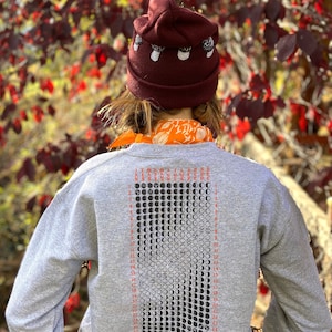K&ouml;nnte beinhalten: Ein graues Sweatshirt mit einem schwarz-wei&szlig;en Mondphasenkalender, der auf der R&uuml;ckseite aufgedruckt ist. Der Kalender zeigt die Mondphasen f&uuml;r jeden Tag des Monats. Das Sweatshirt hat eine kastanienbraune M&uuml;tze mit wei&szlig;en Pilz-Akzenten oben.