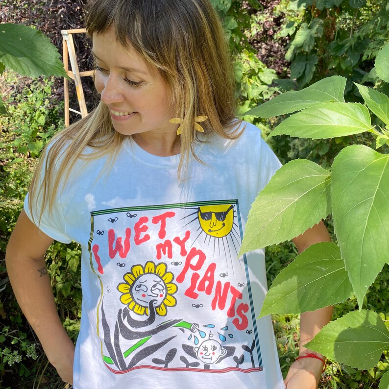 May include: White t-shirt with a graphic of a sunflower with sunglasses and the text "I Wet My Plants".