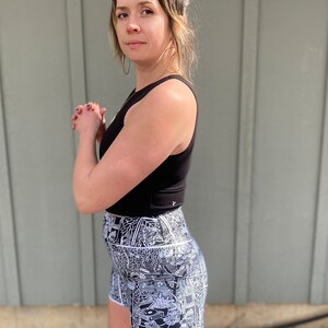 May include: A woman wearing a black tank top and black and white patterned high-waisted shorts. The shorts have a white outline and a complex, detailed design.