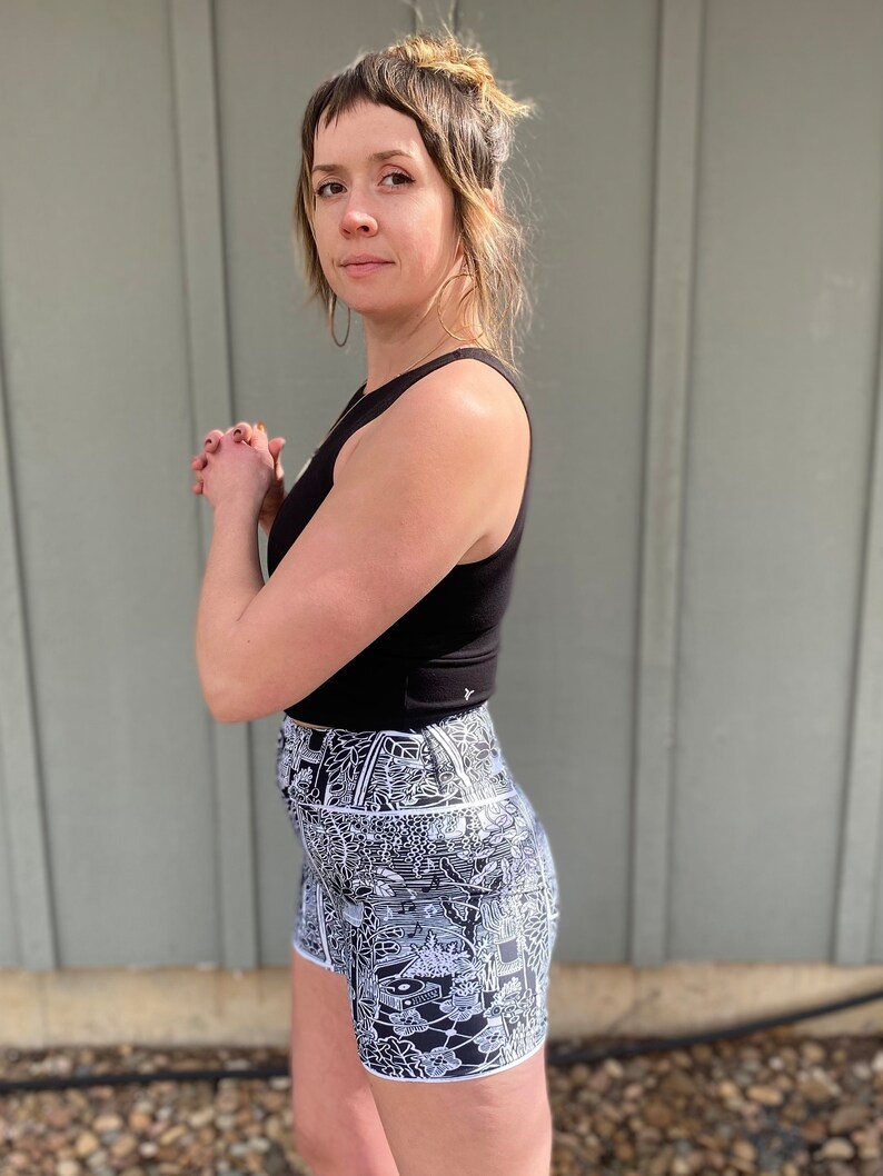 May include: A woman wearing a black tank top and black and white patterned high-waisted shorts. The shorts have a white outline and a complex, detailed design.