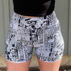 May include: Black and white patterned athletic shorts with a high waist and a graphic print of plants, furniture, and other objects.