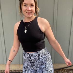 May include: A woman wearing a black tank top and black and white patterned high-waisted shorts. The shorts have a white outline and a variety of abstract designs.