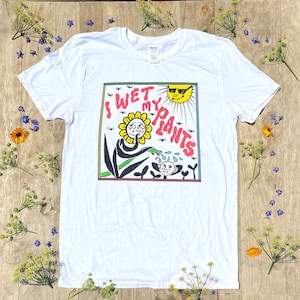 May include: White t-shirt with a cartoon illustration of a flower watering a plant with the text "I WET MY PLANTS" in a rainbow colored box.