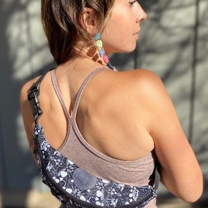 May include: A black fanny pack with a white and black psychedelic mushroom print. The fanny pack has a zipper closure and an adjustable strap.