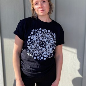 May include: A black t-shirt with a white floral design featuring a circular pattern of flowers, leaves, and butterflies.