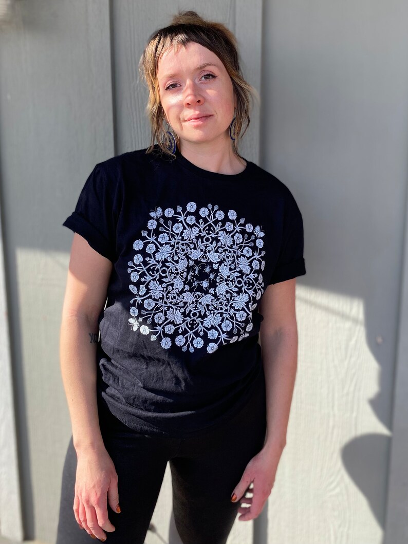 May include: A black t-shirt with a white floral design featuring a circular pattern of flowers, leaves, and butterflies.